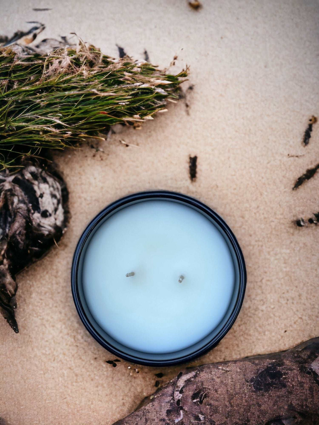 White candle on beach next to driftwood and seaweed